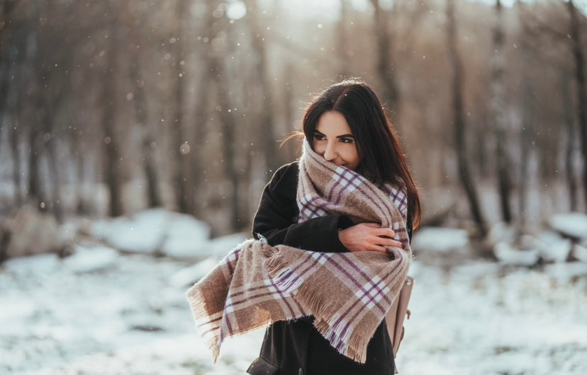 mujer morena en el bosque con nieve tapándose con una bufanda de cuadros