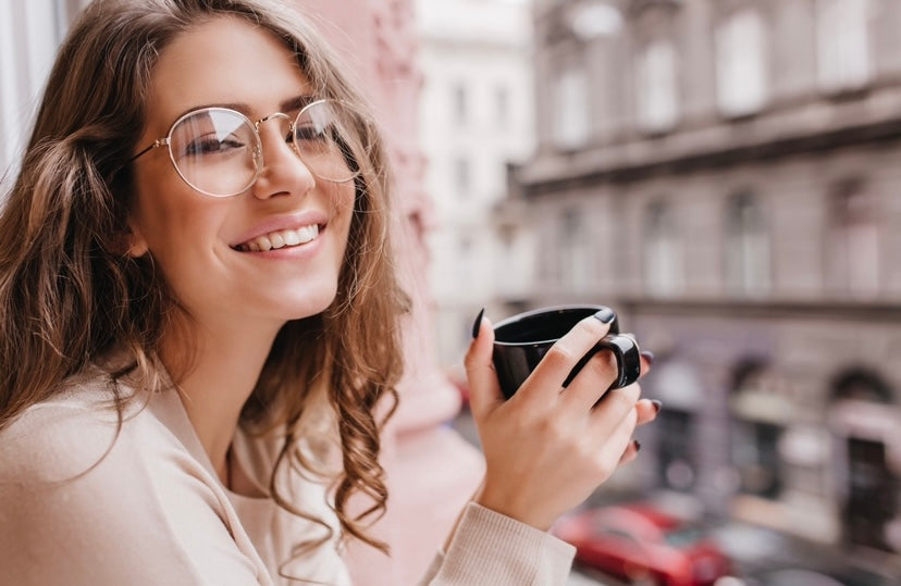 mujer joven con gafas sonriendo feliz asomada  al balcón con una taza en la mano