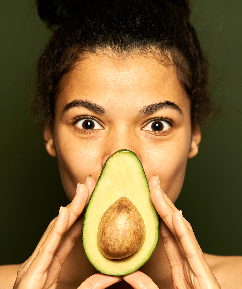 mujer joven morena con medio aguacate delante de la cara