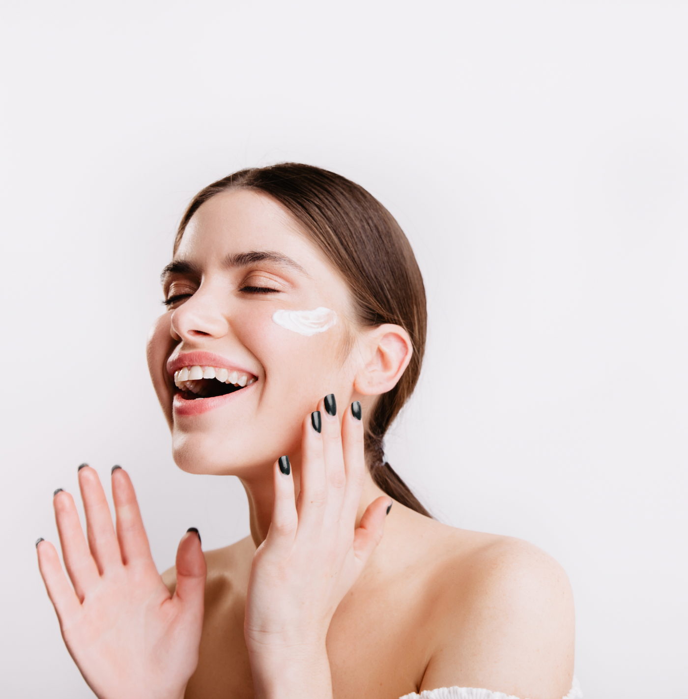 Mujer joven pelo castaño sonriendo con crema en la cara