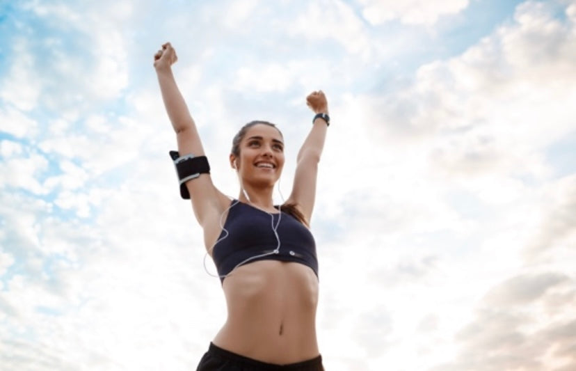 mujer joven deportista con top negro levantando los brazos triunfante fondo cielo con nubes