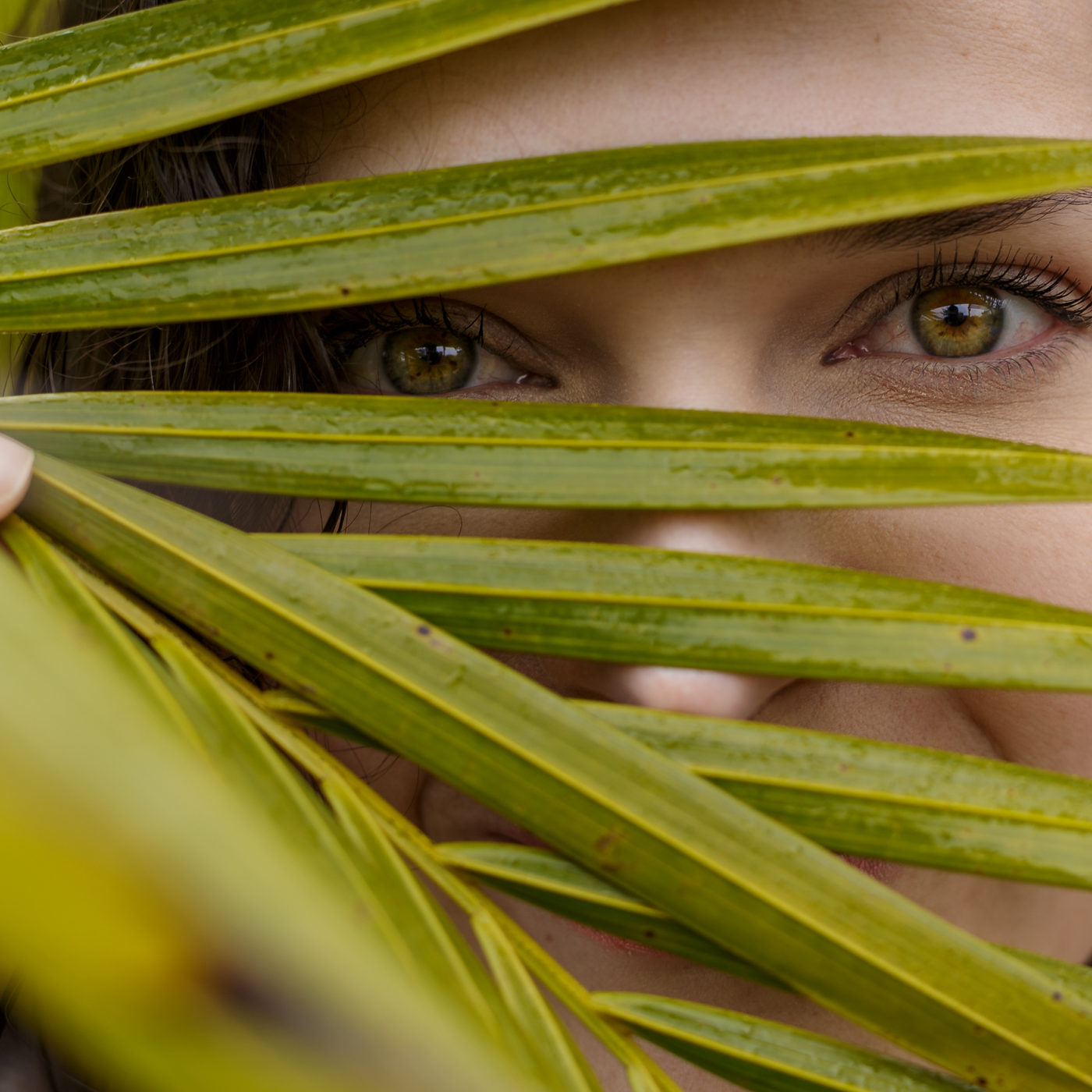 Mujer con piel radiante mirando a través de una hoja grande – Belleza natural y skincare vegano