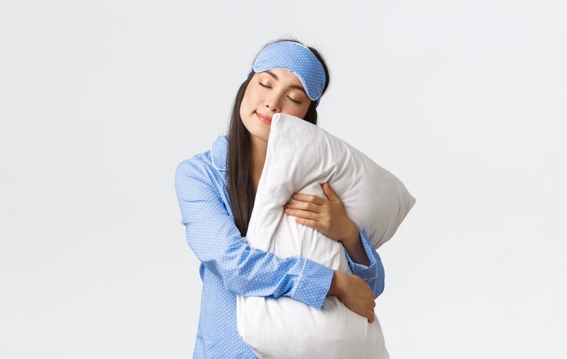 mujer morena con antifaz en la cabeza abrazada a una almohada fondo blanco
