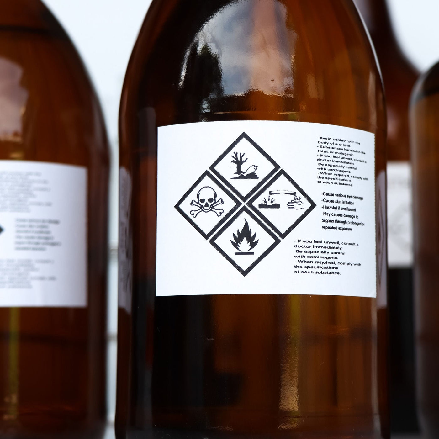 Botellas ámbar con etiquetas de peligro químico (calavera, pez muerto, llamas) que representan ingredientes tóxicos como el fenoxietanol en cosméticos.