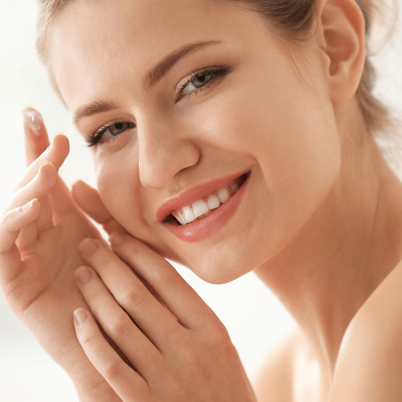 Mujer sonriente tocándose la cara con satisfacción, mostrando piel cuidada y natural, después de aliviar el estrés cutáneo.