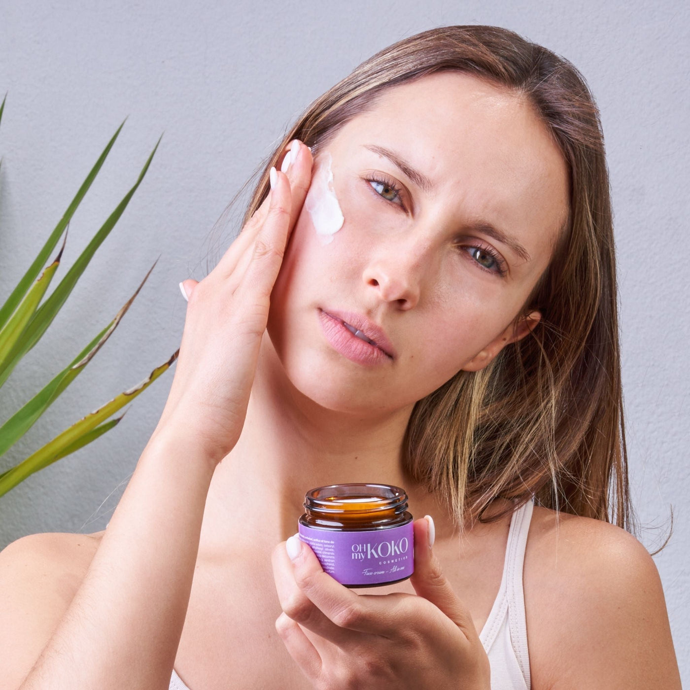 Modelo feliz aplicando la crema facial All in One de OhMyKoko, hidratante natural para todas las pieles que no tapona los poros ni provoca sudor en la cara
