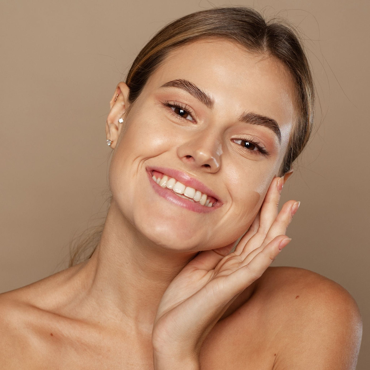 Mujer joven sonriente tocándose la cara, mostrando piel saludable y radiante gracias al cuidado facial natural de OhMyKoko