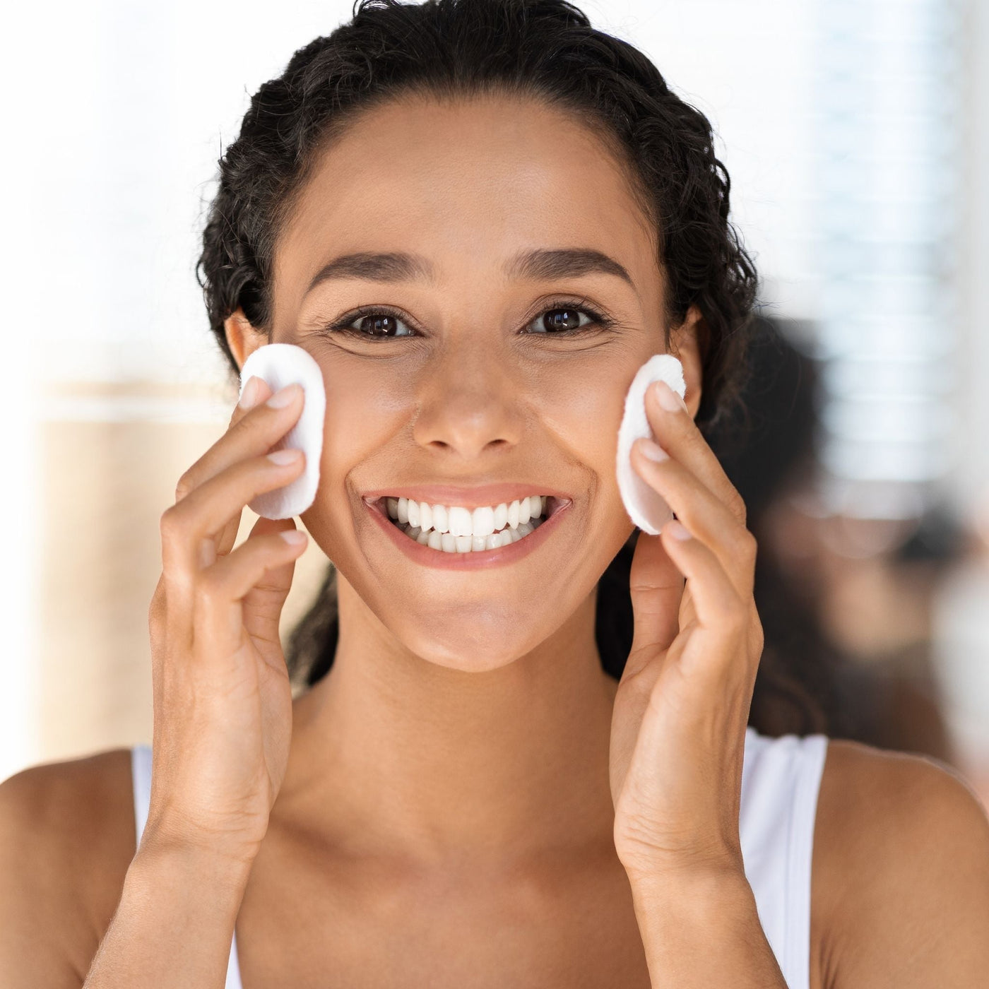 Mujer morena limpiándose el rostro con discos desmaquillantes naturales, disfrutando de una rutina de cuidado facial vegana y suave