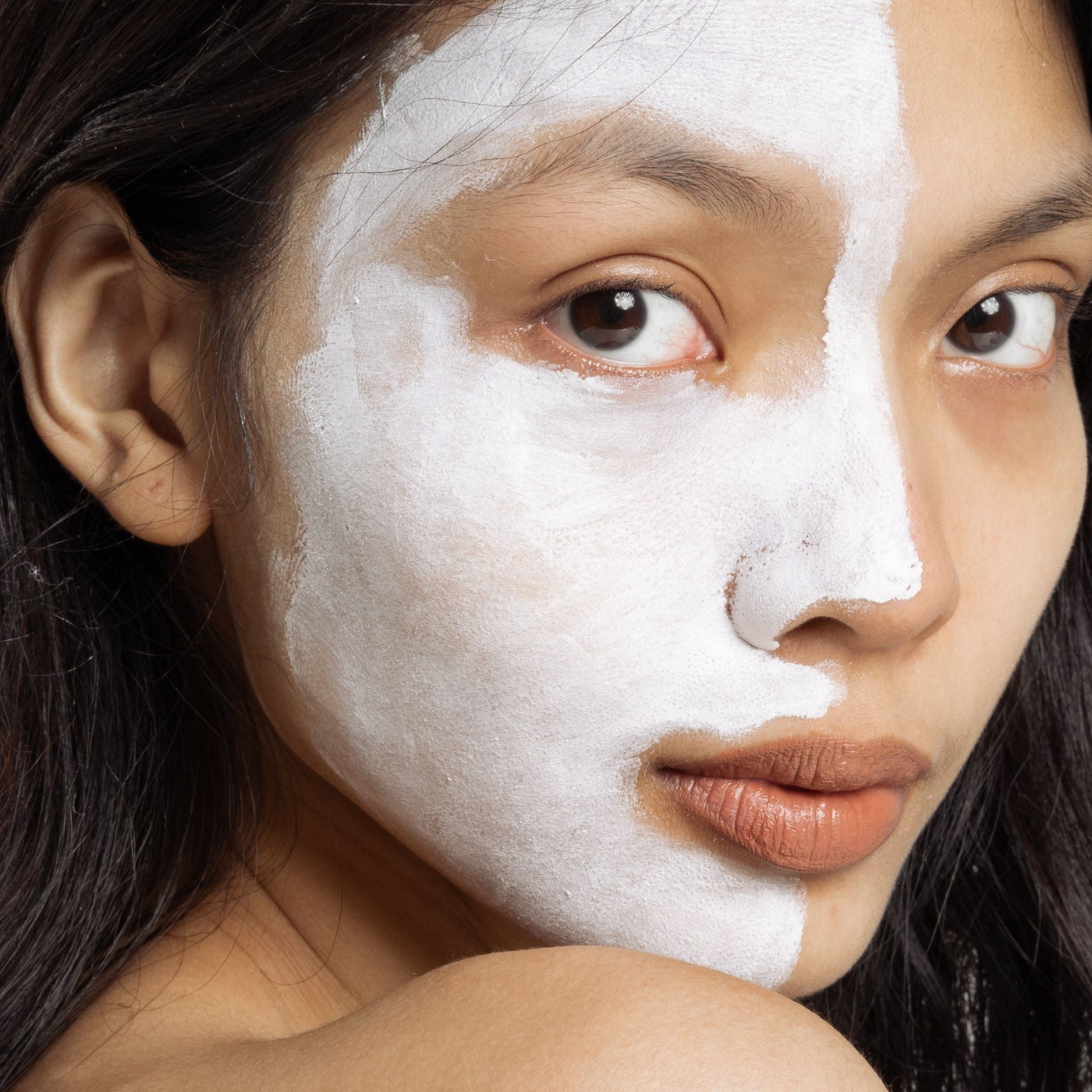 Medio rostro de mujer oriental con crema facial natural aplicada en la piel, mostrando el contraste entre piel tratada y piel natural, representando el cuidado facial natural y minimalista de OhMyKoko.